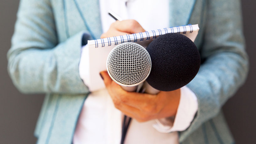 Person holding microphones and taking notes, symbolizing interview and information gathering.