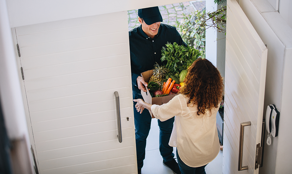 Eine Frau nimmt eine Lieferung von frischem Obst und Gemüse an ihrer Haustür entgegen.
