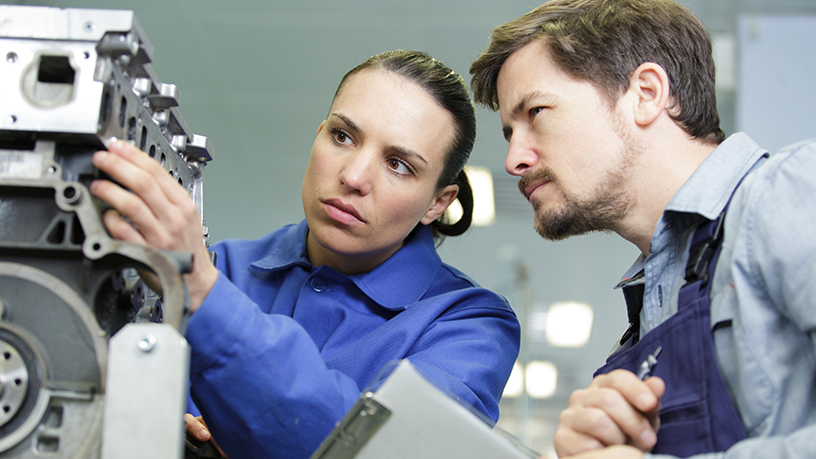 Zwei Personen arbeiten zusammen an einem Motorblock und besprechen die Schritte zur Reparatur.