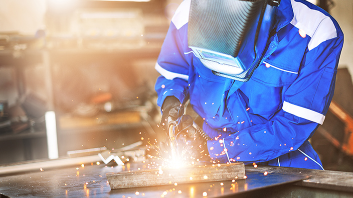 Schweißer mit Schutzmaske bearbeitet Metall unter Funkenflug, zeigt Schweißtechnik und Ausbildung.