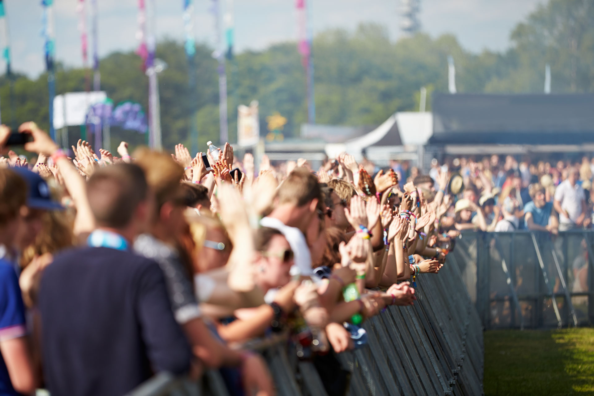 Menschenmenge bei einem Open-Air-Konzert mit erhobenen Händen und Absperrung im Vordergrund
