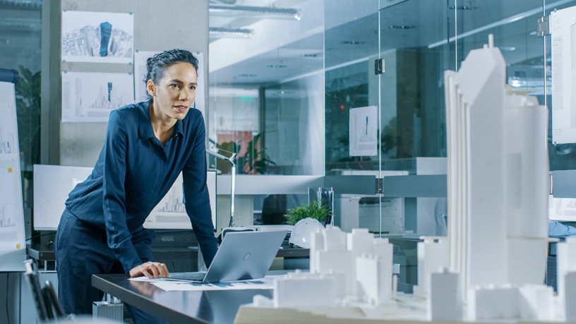 Person in Büro mit Architekturmodellen und Laptop.