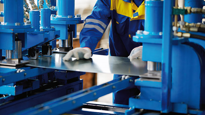 Arbeiter in Schutzkleidung bedient Maschine gemäß Maschinenrichtlinie für Sicherheit.
