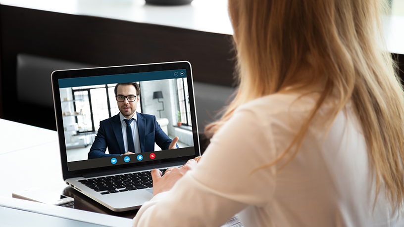 Frau sitzt am Tisch und führt ein Videomeeting auf einem Laptop.