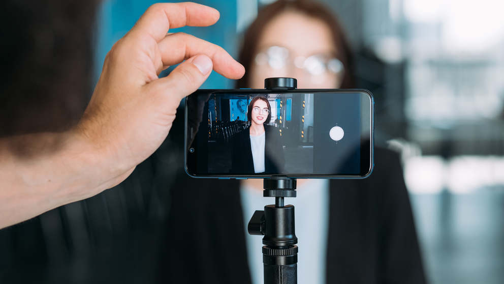 Eine Hand passt ein Smartphone auf einem Stativ an, für die Videoaufnahme in einem modernen Innenraum.