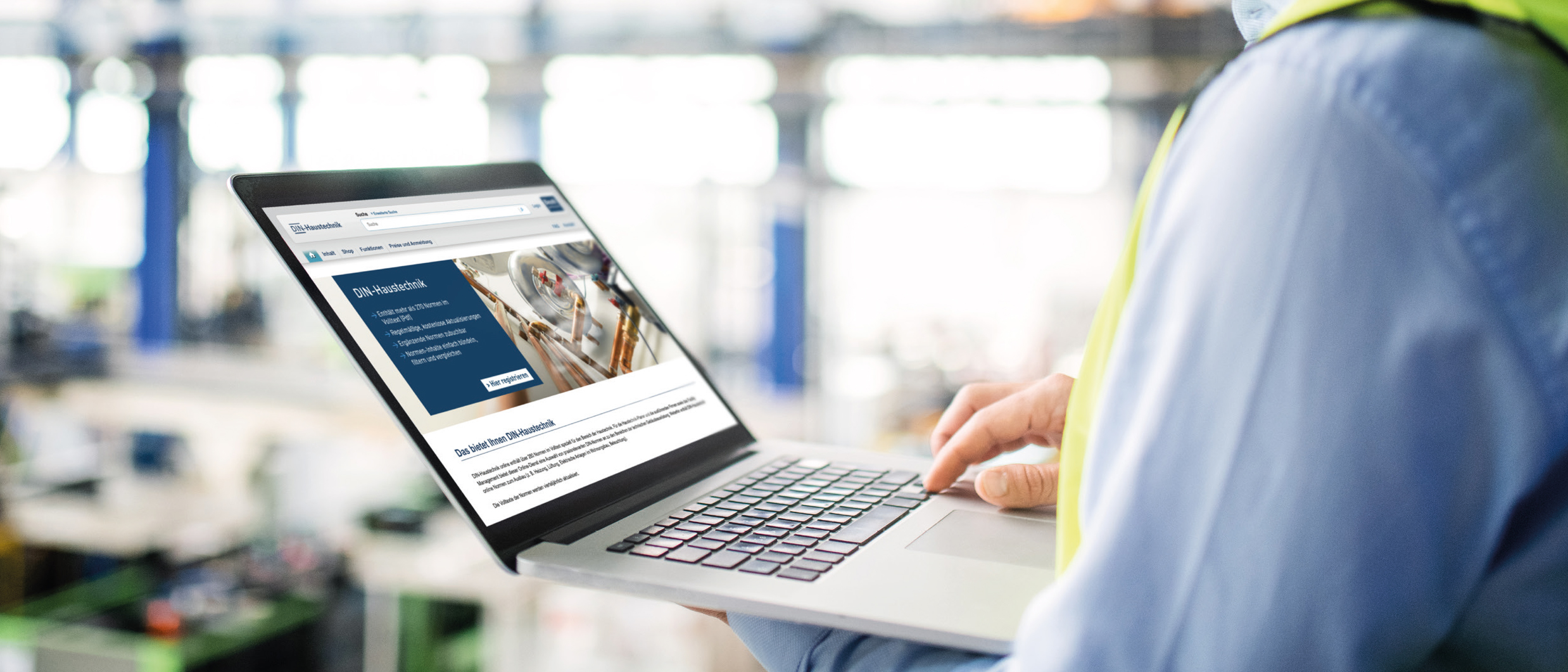 Person in Arbeitskleidung nutzt Laptop mit Webseite über DIN-Haustechnik in industrieller Umgebung.