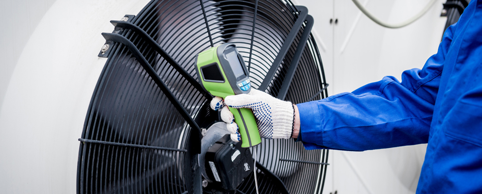 Techniker in blauer Arbeitskleidung misst mit einem Handgerät die Temperatur einer Wärmepumpe.