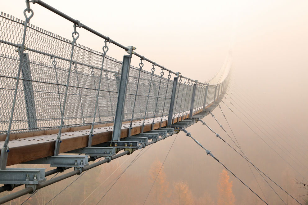 Hängebrücke in Nebel gehüllt, mit Geländern auf beiden Seiten.