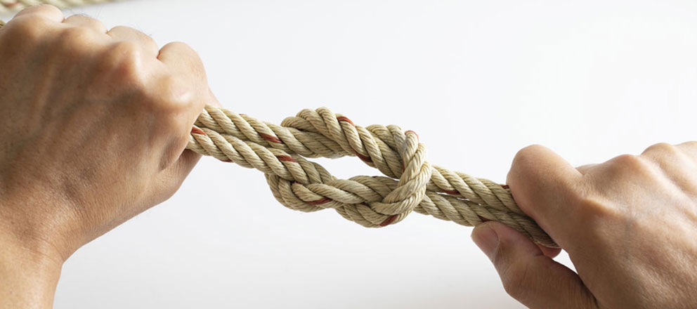 Hände ziehen an einem Seil mit Knoten auf weißem Hintergrund