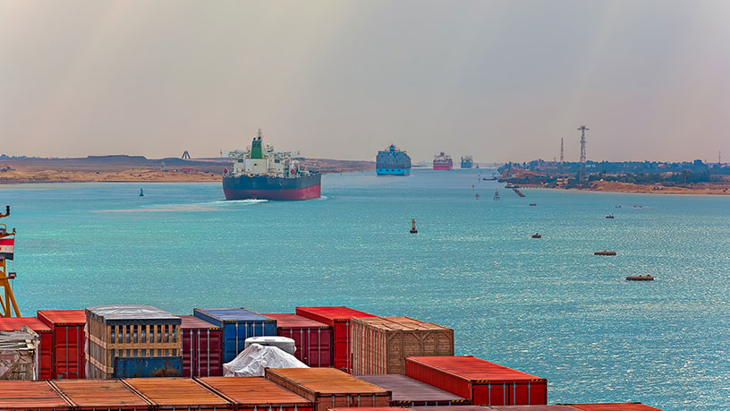 Große Containerschiffe fahren durch einen Kanal, umgeben von Wasser und Landschaft.