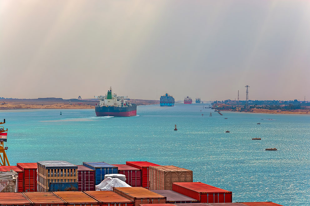 Containerschiffe in einer Wasserstraße, umgeben von blauem Wasser und Küstenlandschaft.