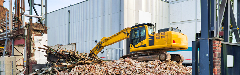 Gelber Bagger auf einem Schuttberg, der Holzreste auf einer Baustelle aufgreift.