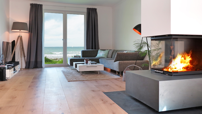 Modernes Wohnzimmer mit Kamin, großen Fenstern und Meerblick, ausgestattet mit Sofa und Stehlampe.