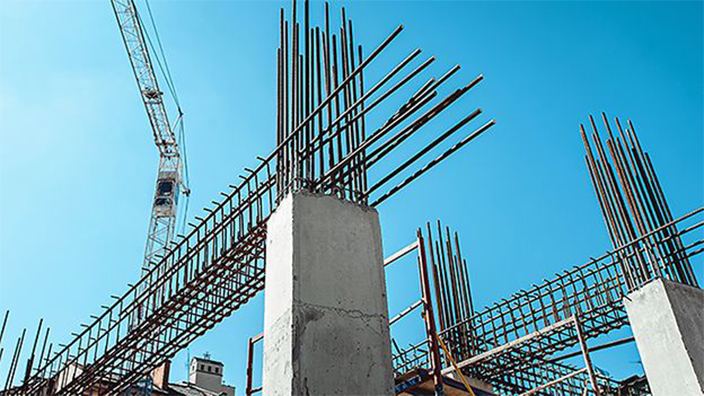 Baustelle mit Betonpfeilern und Stahlarmierungen unter klarem Himmel.