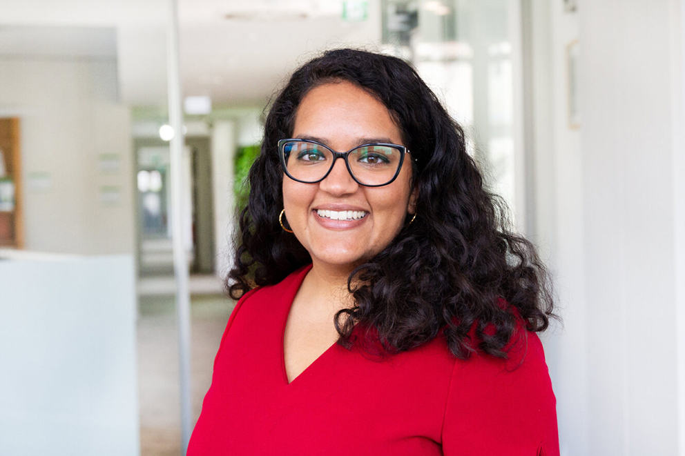 Seema Issar in rotem Oberteil in einem Büro-Umfeld.