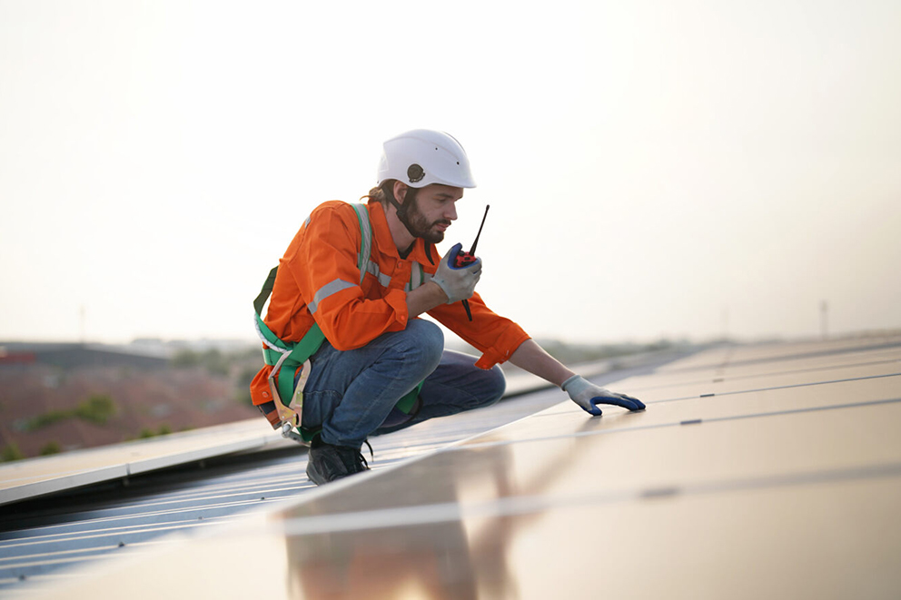 Techniker in Sicherheitskleidung prüft Solarpaneele auf einem Dach.