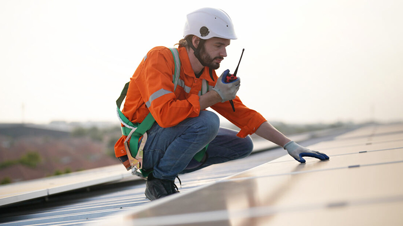 Techniker in Sicherheitskleidung prüft Solarpaneele auf einem Dach.