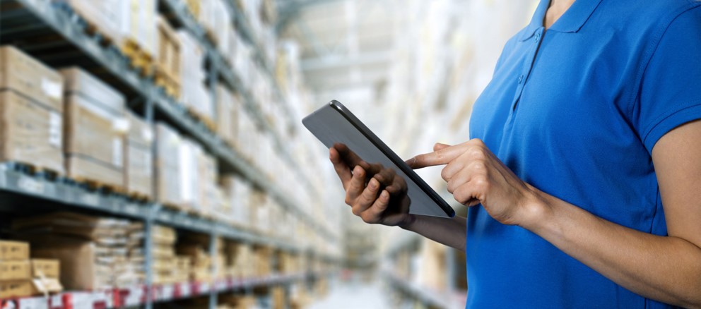 Person in blauem Shirt verwendet ein Tablet in Lagerumgebung.