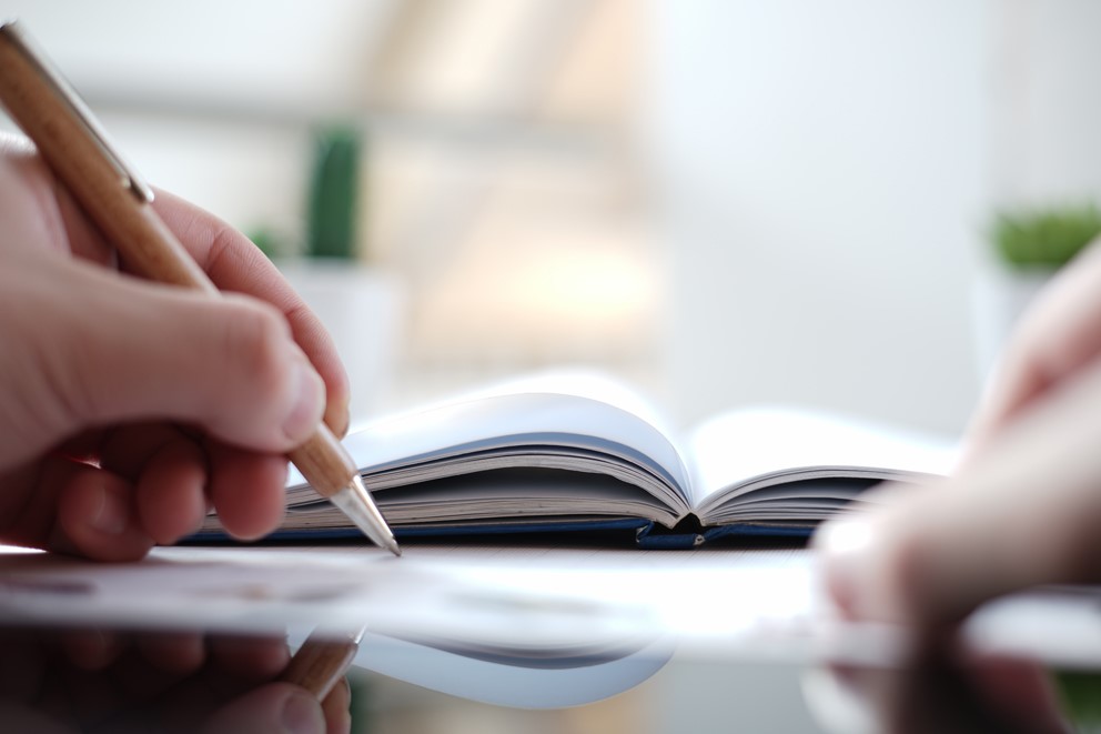 Person schreibt mit Stift in ein aufgeschlagenes Notizbuch.