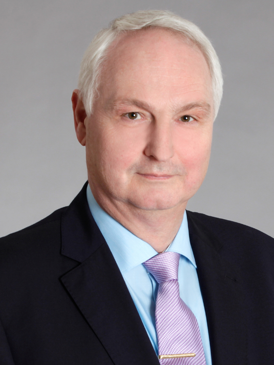 Dr. Frank Herdmann in Anzug mit hellblauem Hemd und lavendelfarbener Krawatte.