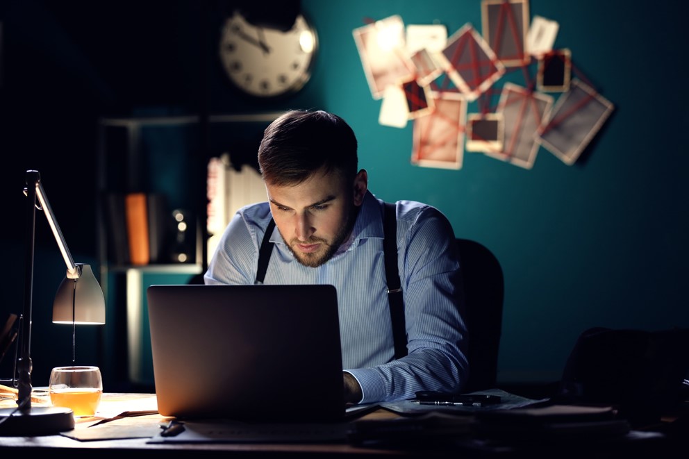 Person arbeitet nachts am Laptop, mit Getränk auf dem Schreibtisch.