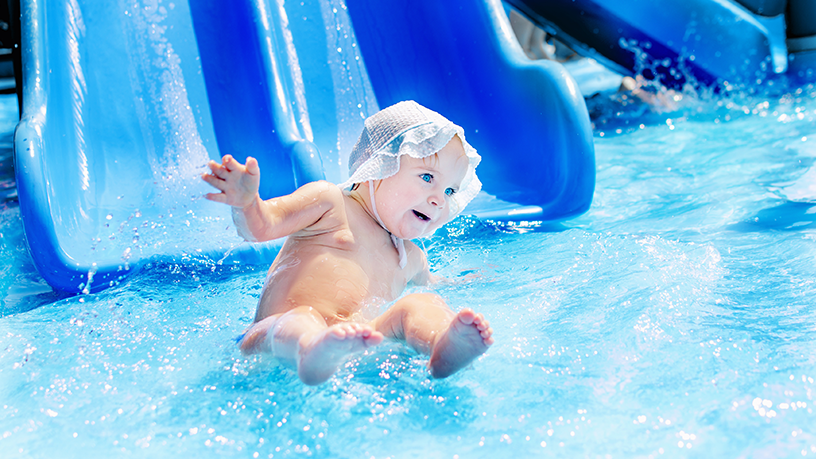 Ein Baby rutscht eine blaue Wasserrutsche hinunter in ein Becken.