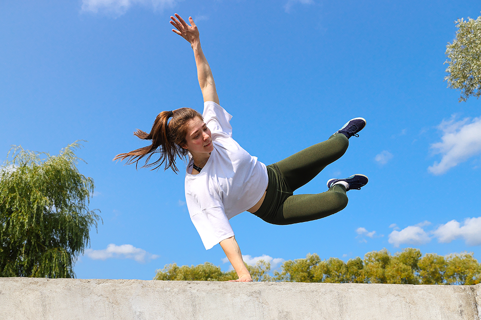 Person springt dynamisch auf einer Mauer, mit ausgestrecktem Arm.