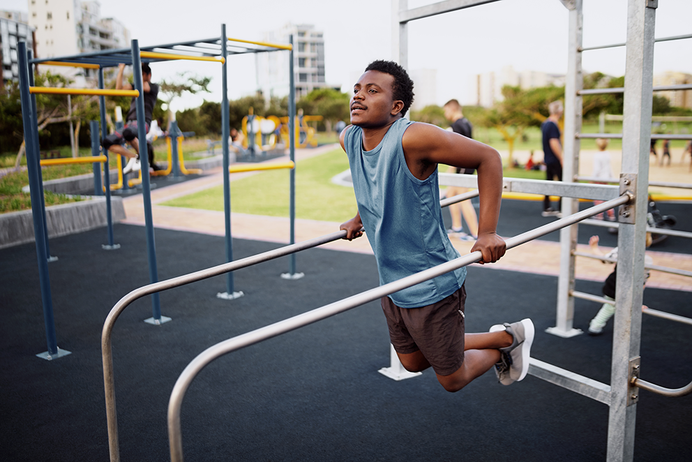 Person macht Klimmzüge an parallelen Stangen im Outdoor-Fitnessbereich.
