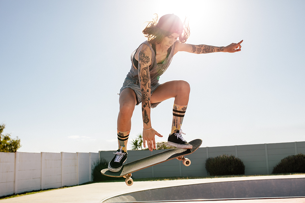 Tätowierte Person beim Skateboard-Trick im Skatepark.
