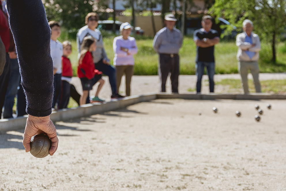 Person beim Boulespiel mit Zuschauern im Hintergrund.