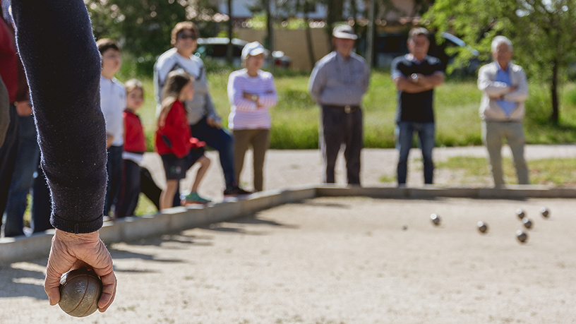 Person beim Boulespiel mit Zuschauern im Hintergrund.