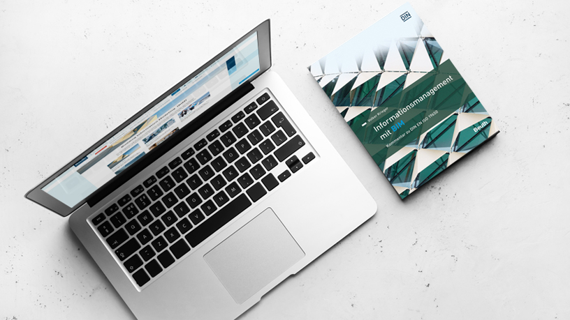Ein geöffneter Laptop auf einem hellen Tisch neben dem Buch "Informationsmanagement mit BIM".