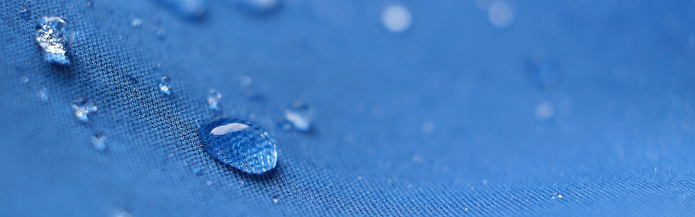 Wassertropfen auf blauem, wasserabweisendem Gewebe in Nahaufnahme.