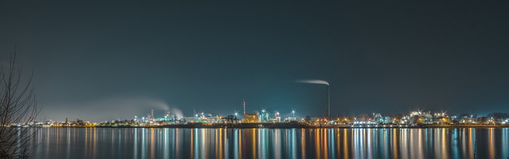 Beleuchtete Industrieanlage bei Nacht mit Spiegelung im Wasser.