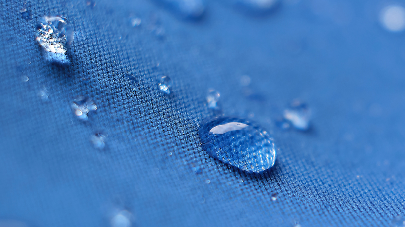 Nahaufnahme von Wassertropfen auf blauer wasserabweisender Oberfläche.