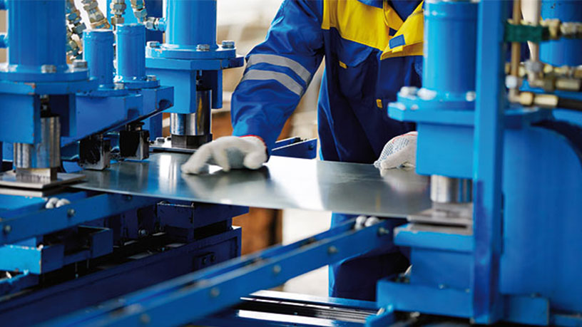 Ein Arbeiter in blauer Schutzkleidung und weißen Handschuhen bedient eine Metallpresse.