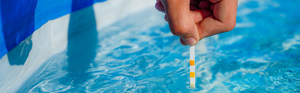 Eine Hand hält einen Teststreifen ins Poolwasser, um die Wasserqualität zu überprüfen.