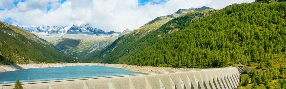 Staudamm mit See, umgeben von Bergen und Wäldern.