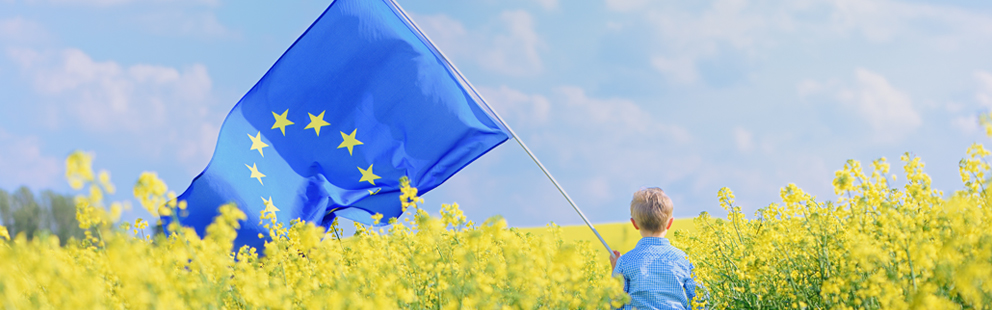 Kind in einem blühenden Feld mit EU-Flagge.