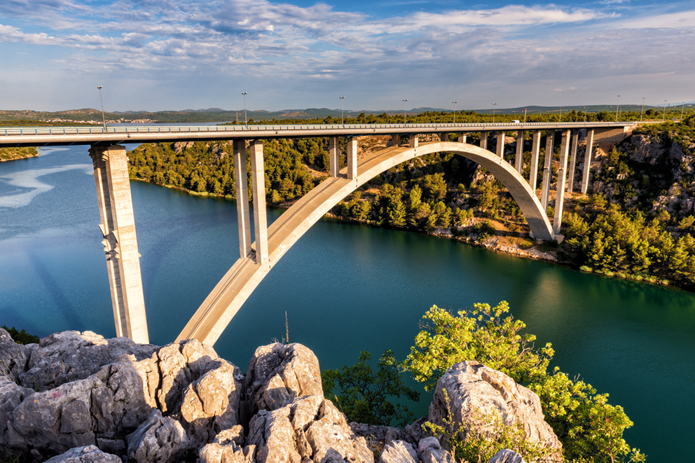 Große Bogenbrücke über einem Fluss, umgeben von grüner Landschaft.