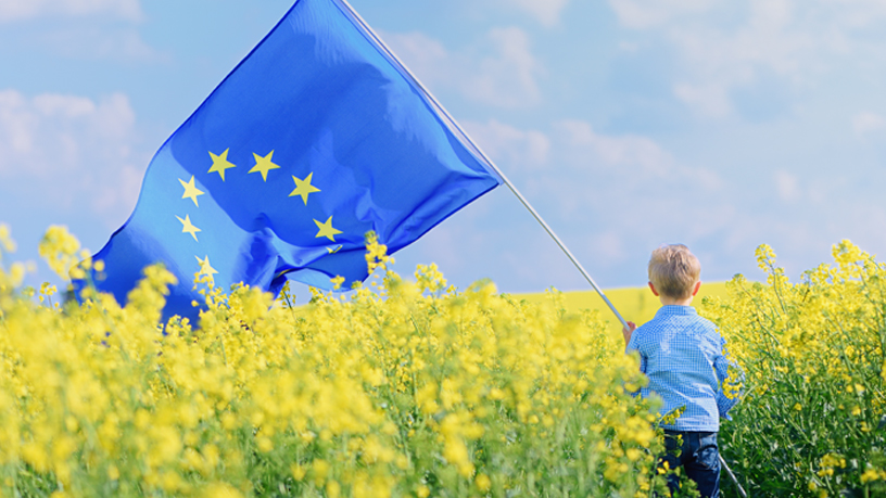 Kind mit Europaflagge in blühendem Feld symbolisiert nachhaltige Kreislaufwirtschaft durch EU-Initiativen.