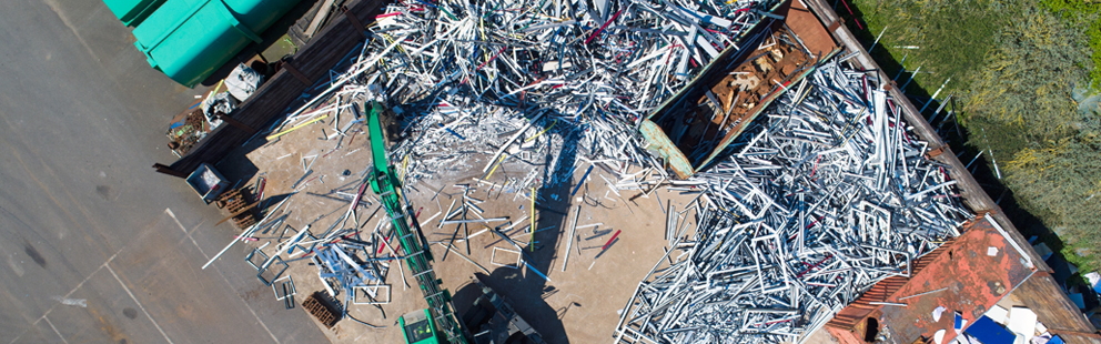 Luftaufnahme einer Recycling-Anlage mit einem Kran, der Metallteile bewegt.