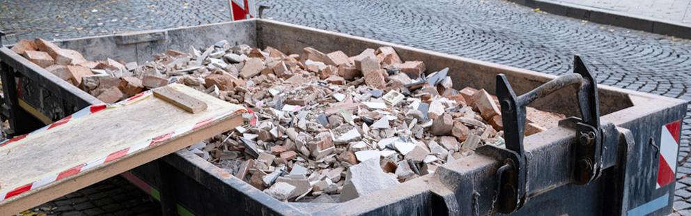 Container voller Ziegel und Bauschutt auf gepflasterter Straße.