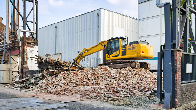 Bagger steht auf einem Haufen aus Schutt und Ziegeln an einer Baustelle.
