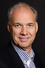 Harald Ackerschott in dunklem Anzug und kariertem Hemd vor dunklem Hintergrund.