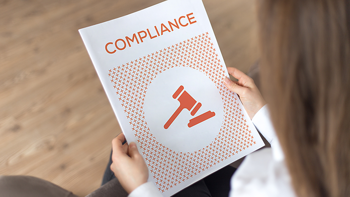 Person hält ein Compliance-Dokument mit einem Richterhammer-Symbol.