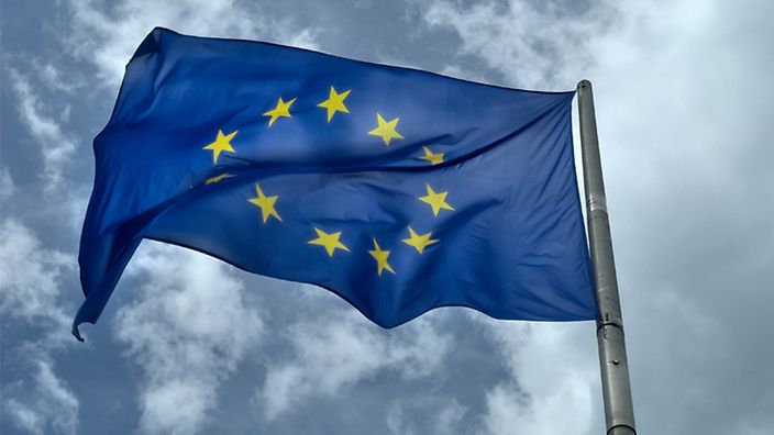 Europäische Union Flagge weht vor bewölktem Himmel.