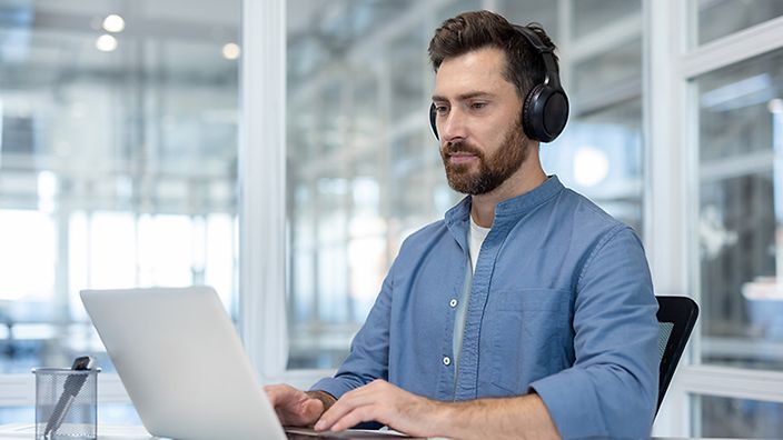 Mann am Schreibtisch und Laptop mit Kopfhörern 